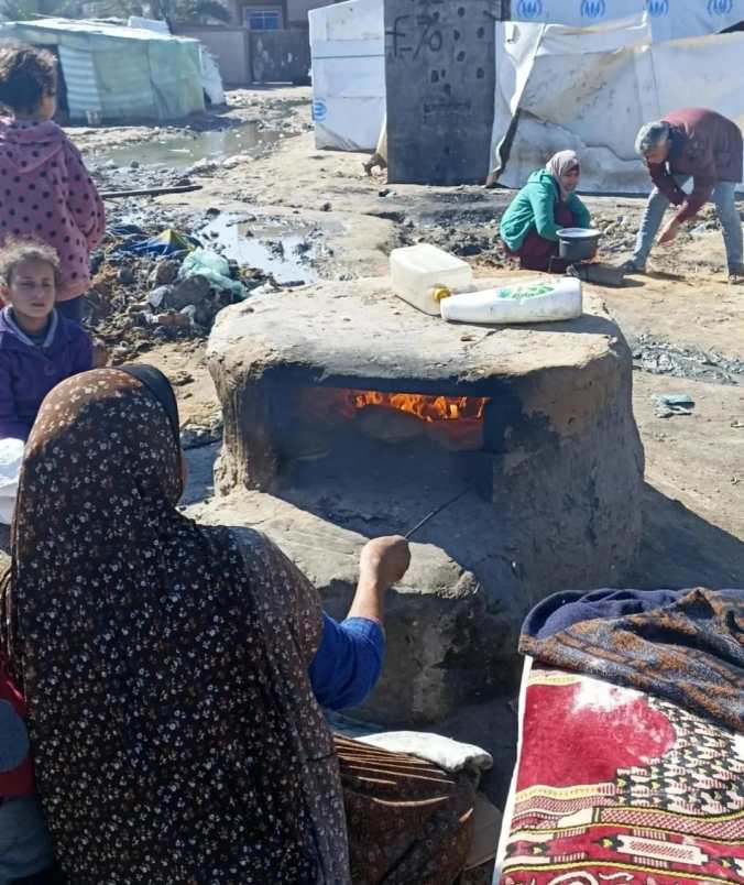 A woman sat baking bread at an outdoor, wood-fueled oven
