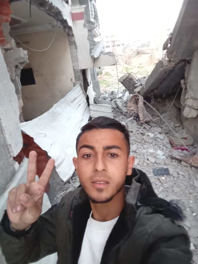 Muhammad standing giving the peace sign in his destroyed house