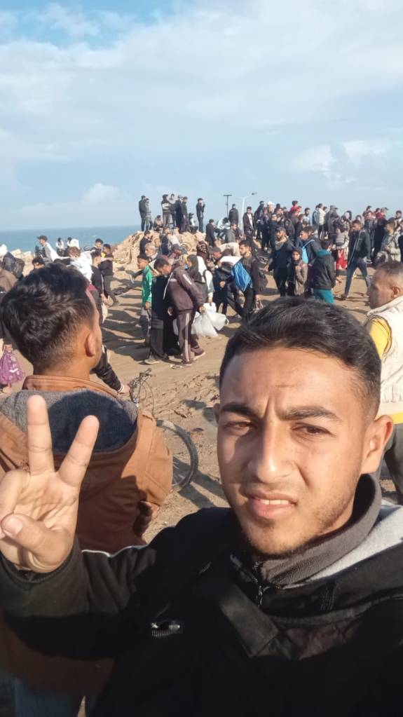 Muhammad walking home to Gaza City and giving the peace sign, among a crowd of displaced Palestinians.