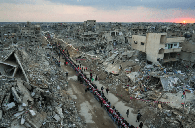 Palestinians in Rafah, southern Gaza, sit at a long table to celebrate Iftar, the fast-breaking meal, on the first day of Ramadan. They sit amid the rubble of destroyed homes.